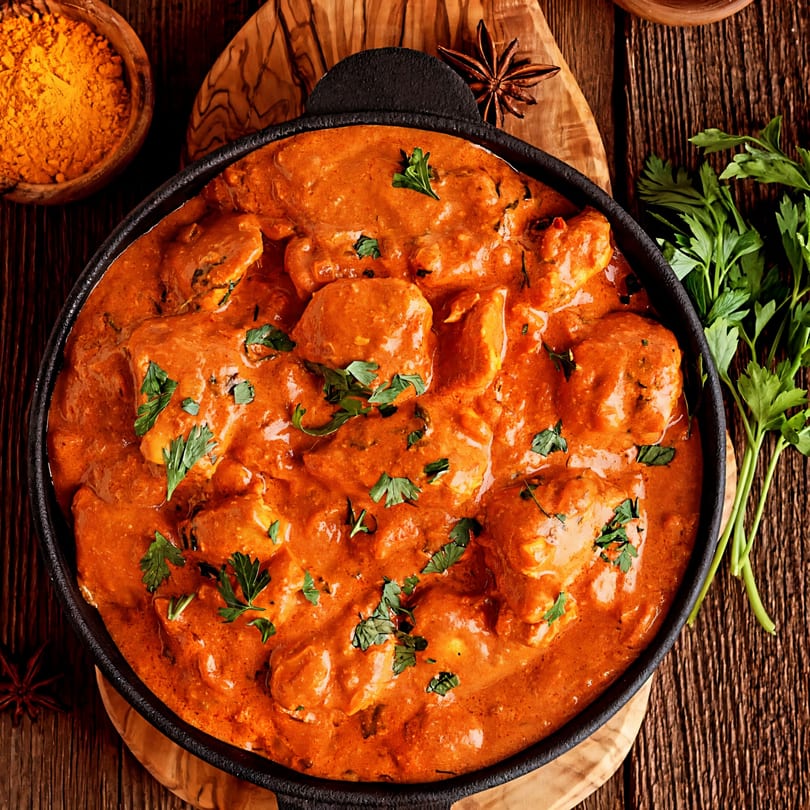 Close-up of Indian butter chicken in a black skillet, garnished with fresh parsley.