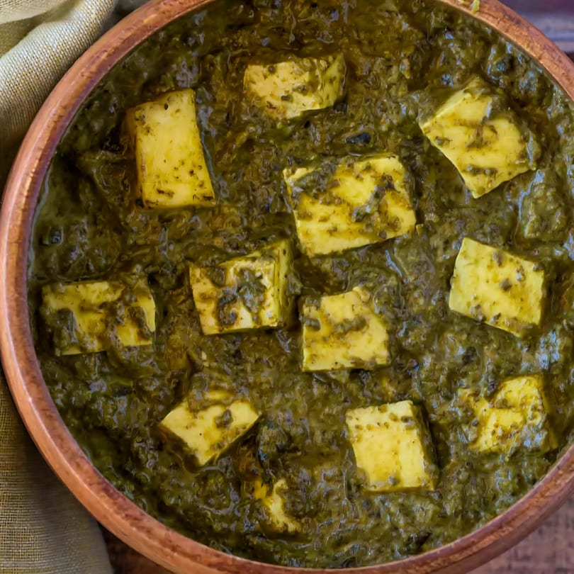 Close-up of Palak Paneer, a vibrant green Indian spinach and cheese curry, in a copper bowl.