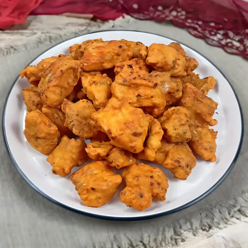 A white plate filled with golden-brown, irregularly shaped Indian pakoras, a popular snack from Flavors Of India.